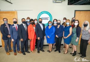 A group of adults standing together wearing masks in front of a sign at Southside Medical Center. They are a mix of Black, White, Latino, and other races.